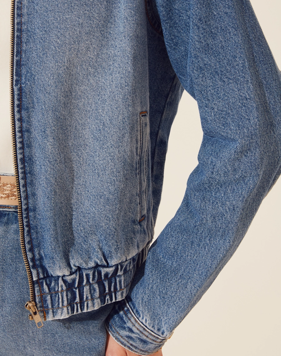 Jaqueta Jeans Bomber confeccionado em jeans. 
Possui gola esportiva, e zíper frontal para fechamento, possui elástico na barra proporcionando conforto e flexibilidade. 
Punhos da manga com botão de casa. 