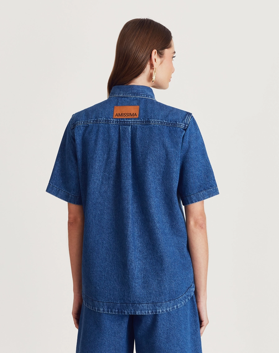 Camisa Bonnie confeccionada em jeans com lavagem escura. Versátil, pode ser usada aberta como sobreposição ou fechada, compondo combinações modernas e despojadas.