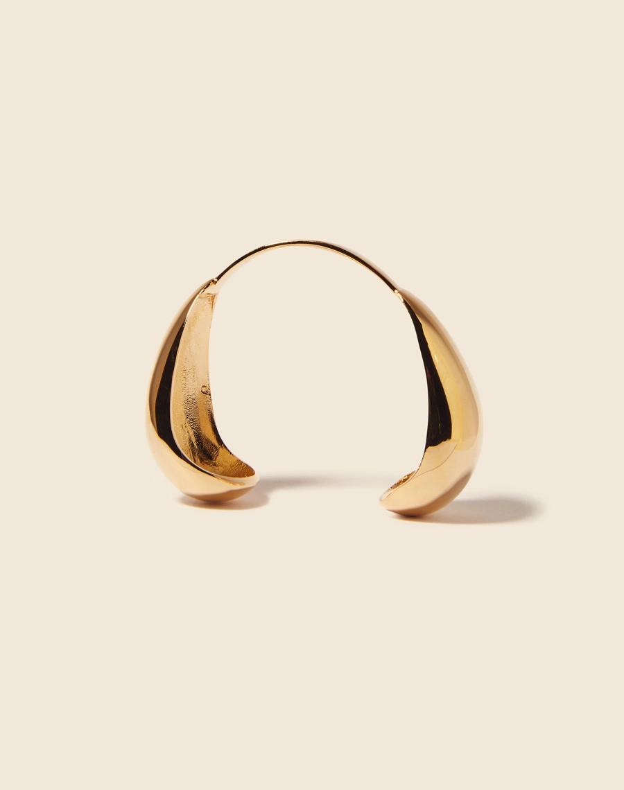 Bracelete ajustado ao pulso, com extremidades simétricas e curvas delicadas. Apresenta um acabamento banhado a ouro, adicionando um toque de sofisticação e brilho.