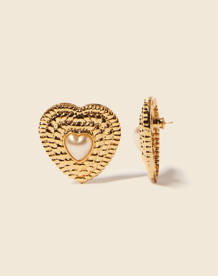 Brincos boucle em forma de coração, delicadamente texturizados e adornados com uma pérola. <br/>
Cada peça é meticulosamente feita à mão e possui um acabamento banhado a ouro. <br/>