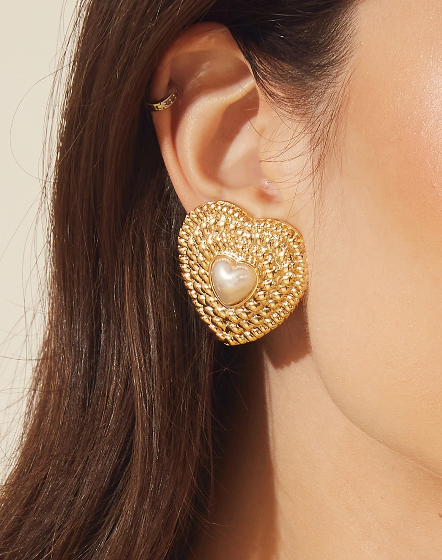 Brincos boucle em forma de coração, delicadamente texturizados e adornados com uma pérola. <br/>
Cada peça é meticulosamente feita à mão e possui um acabamento banhado a ouro. <br/>