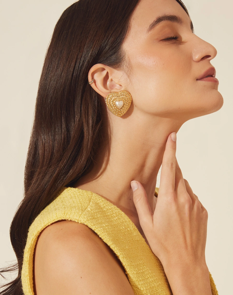 Brincos boucle em forma de coração, delicadamente texturizados e adornados com uma pérola. <br/>
Cada peça é meticulosamente feita à mão e possui um acabamento banhado a ouro. <br/>