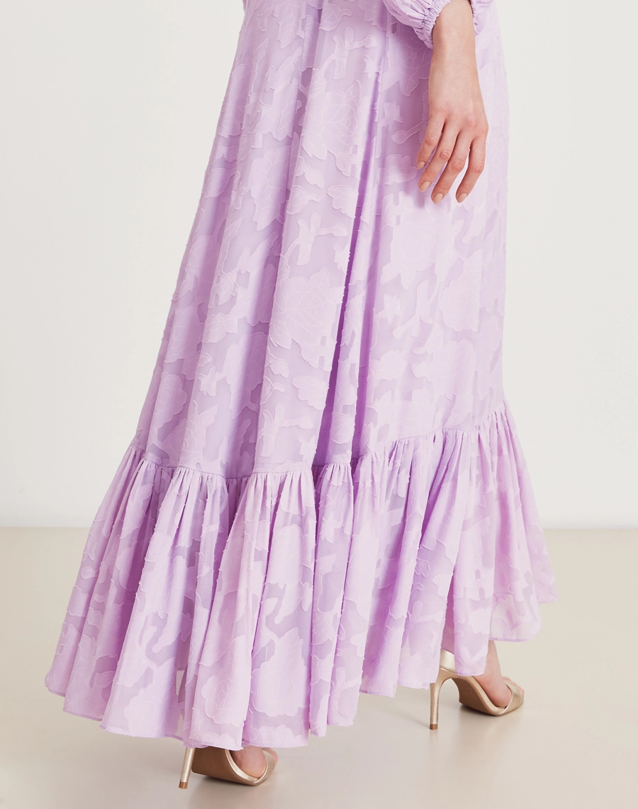 Vestido longo lavanda em jacquard floral com mangas bufantes e babado na barra. Sofisticação e elegância para eventos especiais.