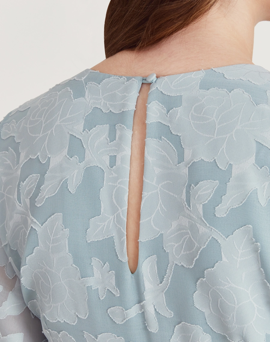 Vestido midi em jacquard floral azul, com mangas bufantes, faixa na cintura e caimento elegante. Ideal para eventos formais.