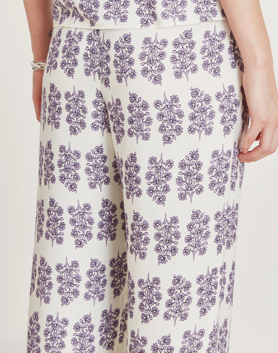 A Calça Lylla é confeccionada em viscose estampada, um tecido leve e suave ao toque, oferecendo leveza e frescor ao vestir. Com estampa floral Amissima exclusiva em tons de roxo sobre fundo claro. 