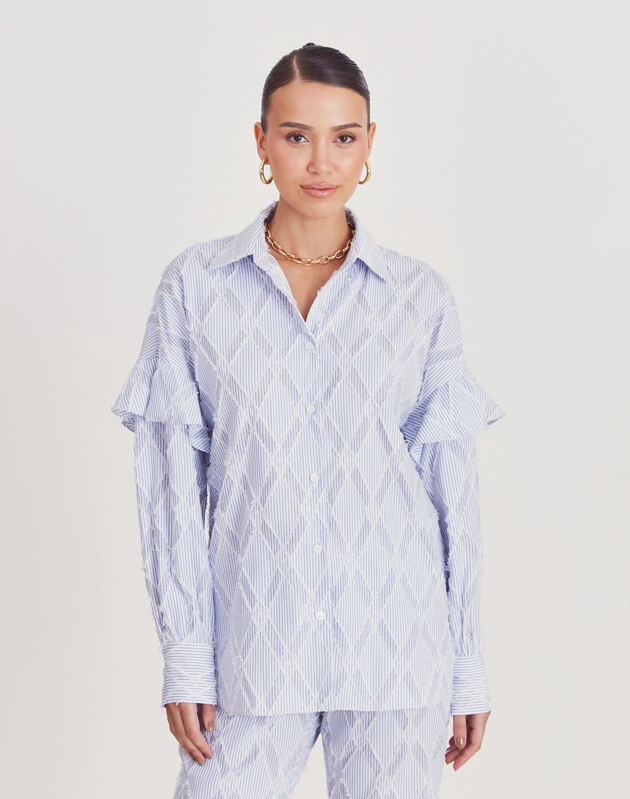 Camisa Jenni confeccionada em cambraia, tecido maquinetado com padrão geométrico em relevo e acabamento desfiado, que confere textura e
toque artesanal à peça.